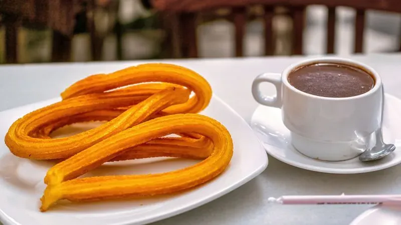 طبق من الشوروز الذهبي مع فنجان من الشوكولاتة الساخنة، يُعتبر من الحلويات التقليدية في إسبانيا.