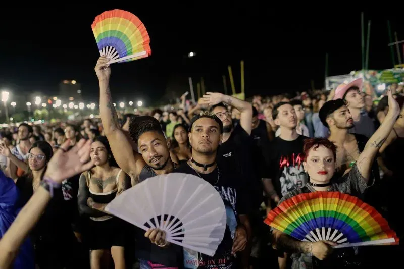 حشود من المعجبين في شاطئ كوباكابانا خلال حفل ليدي غاغا، يحملون مروحات ملونة ويستمتعون بأجواء الاحتفال.