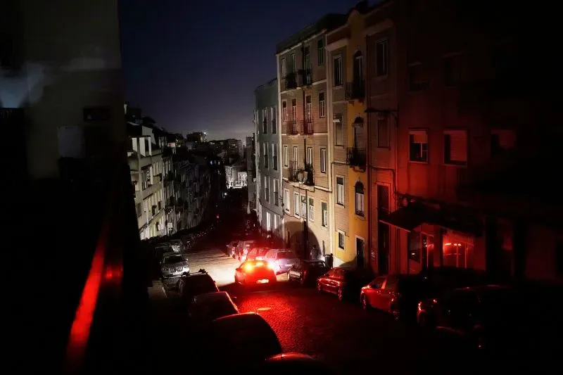 شارع مظلم في مدينة خلال انقطاع الكهرباء، مع وجود سيارات متوقفة وأضواء حمراء لشاحنة طوارئ، مما يعكس حالة الارتباك والقلق.