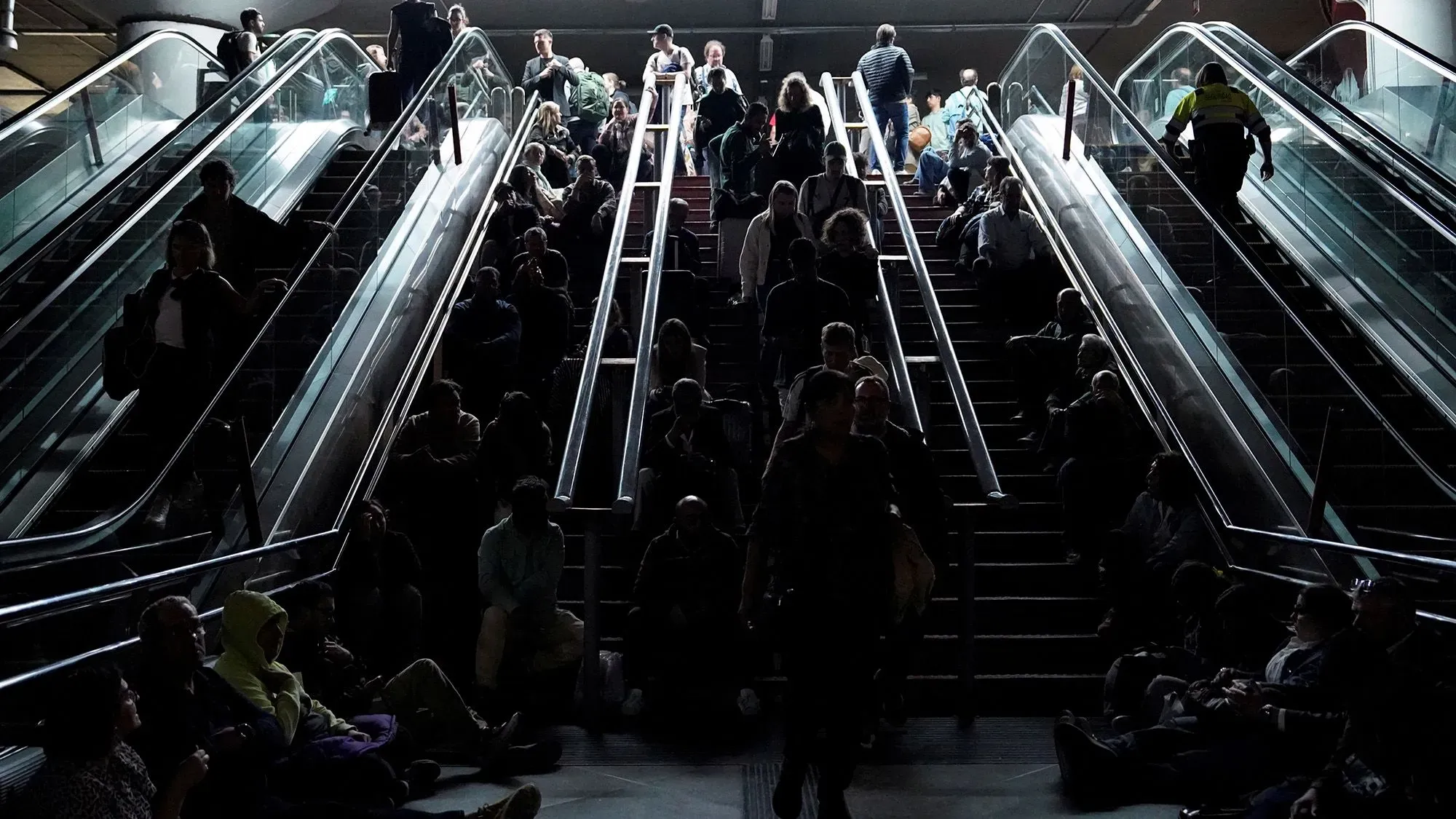 ازدحام كبير في محطة مترو مظلمة، حيث يجلس العديد من الأشخاص على الدرج المتحرك، بينما يتجه آخرون نحو الأعلى، في ظل حالة من الفوضى بعد انقطاع الكهرباء.