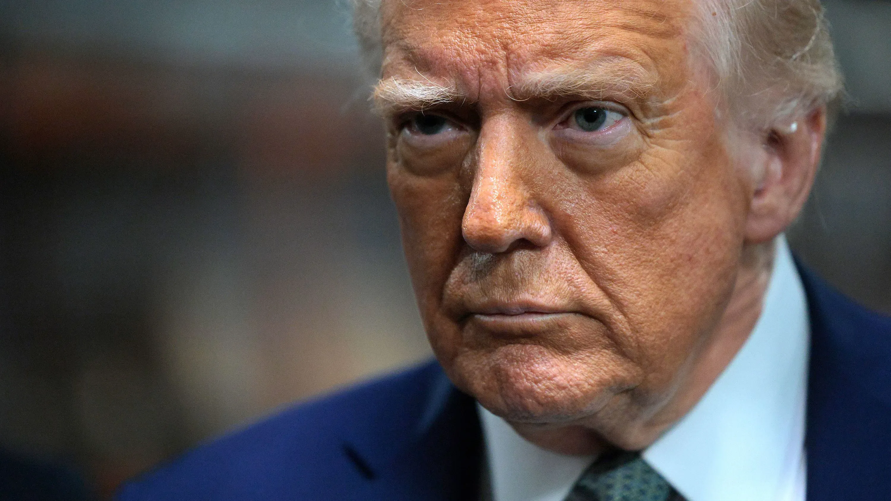 صورة قريبة لوجه الرئيس الأمريكي السابق دونالد ترامب، تعكس تعبيراته الجادة والقلقة خلال حديثه عن قضايا الهجرة وسلطات الرئيس.