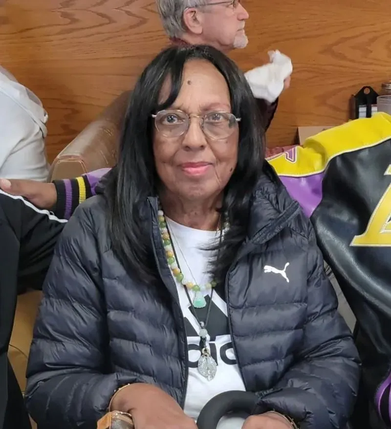 امرأة مسنّة ترتدي سترة داكنة وتبتسم، تجلس في مكان عام مع أشخاص آخرين، تعكس صورة من مجتمعها قبل الحرائق المدمرة في لوس أنجلوس.