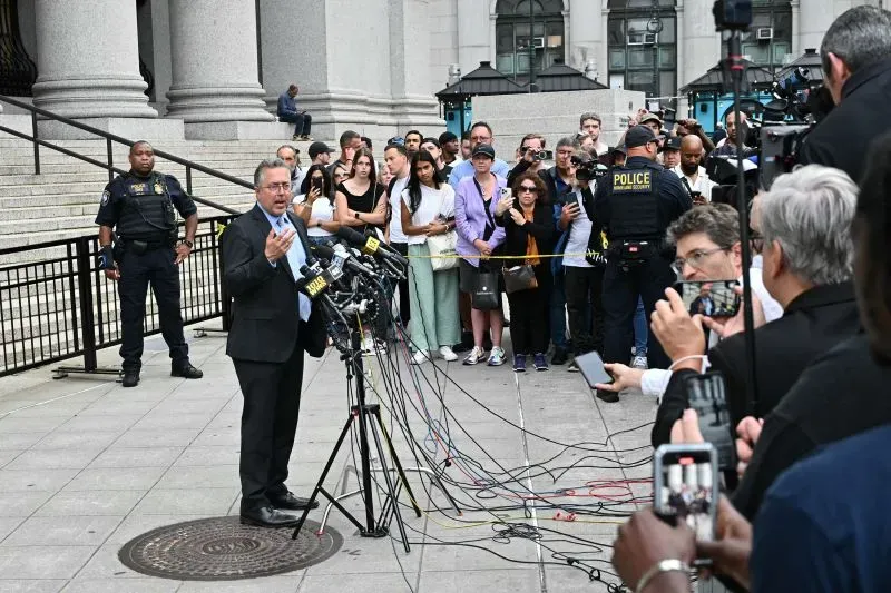 محامي يتحدث أمام حشد من الصحفيين والجمهور خارج المحكمة، مع وجود رجال شرطة في الخلفية. تُظهر الصورة أجواء المحاكمة الجنائية لشون كومبس.