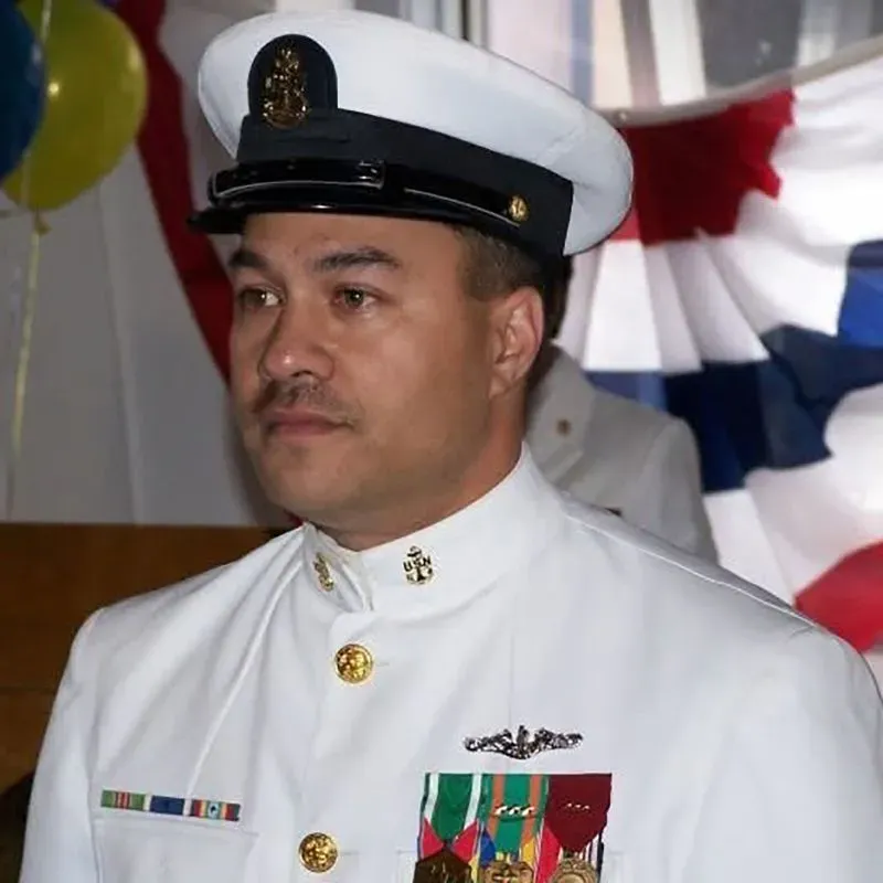 صورة لرجل يرتدي زي البحرية الأمريكية الرسمي، يظهر في خلفية ملونة بأعلام. تعكس الصورة قضية احتجاز زوجين أمريكيين في المكسيك بسبب نزاع قانوني.