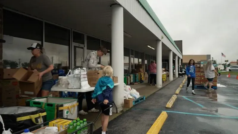 تجمع عائلات في مركز توزيع للمواد الغذائية، حيث يقوم المتطوعون بتوزيع الطعام والمستلزمات الأساسية في أجواء ممطرة.