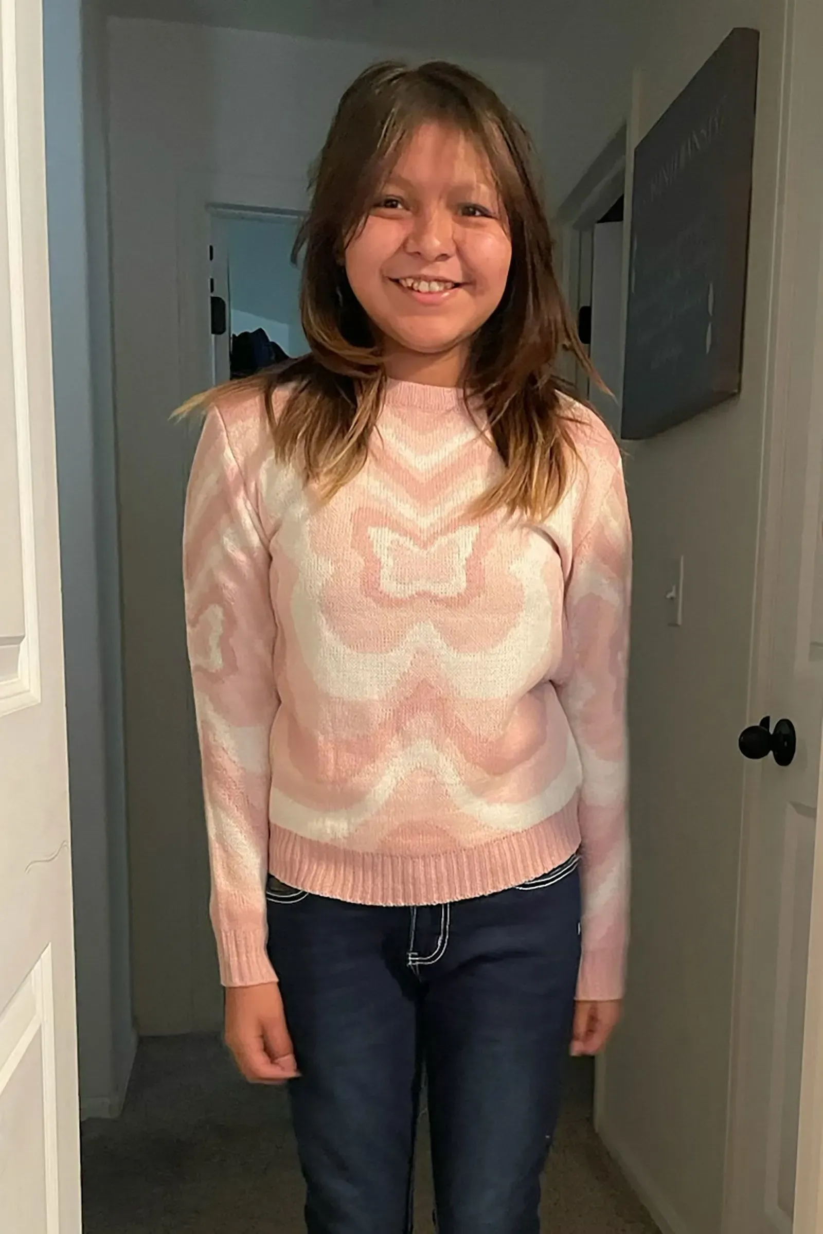 صورة لإيميلي بايك، فتاة من قبيلة سان كارلوس أباتشي، ترتدي سترة وردية وتبتسم، تعكس براءتها وحب عائلتها لها.