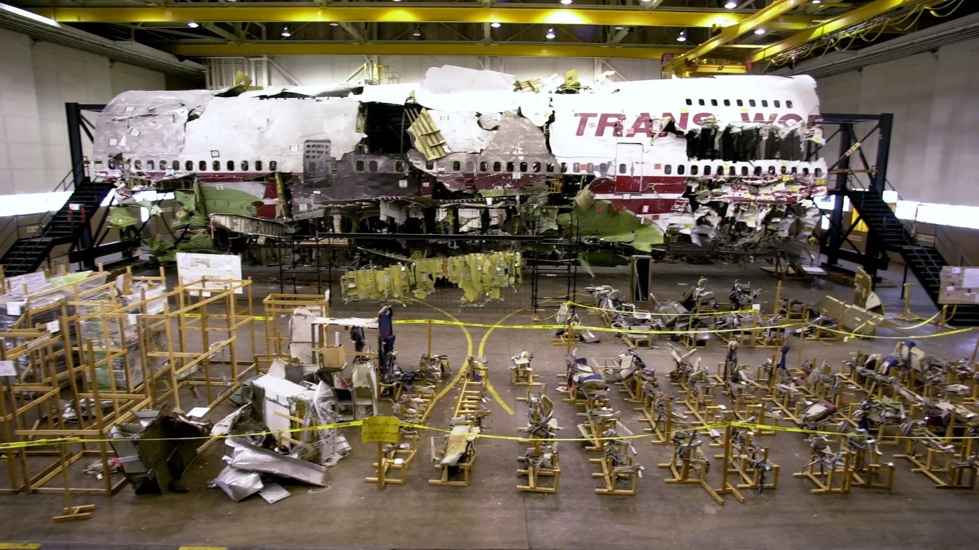 حطام طائرة TWA 800 المعاد بناؤه، يظهر الأجزاء المدمرة في مركز التحقيق، مع وجود أدوات استعادة حوله، بعد الانفجار المأساوي.