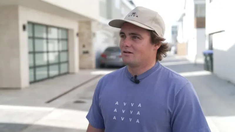 راكب الأمواج لوغان دوليان يتحدث عن تجربته مع السرقة في نيوبورت بيتش، مع خلفية منازل وشوارع المنطقة.