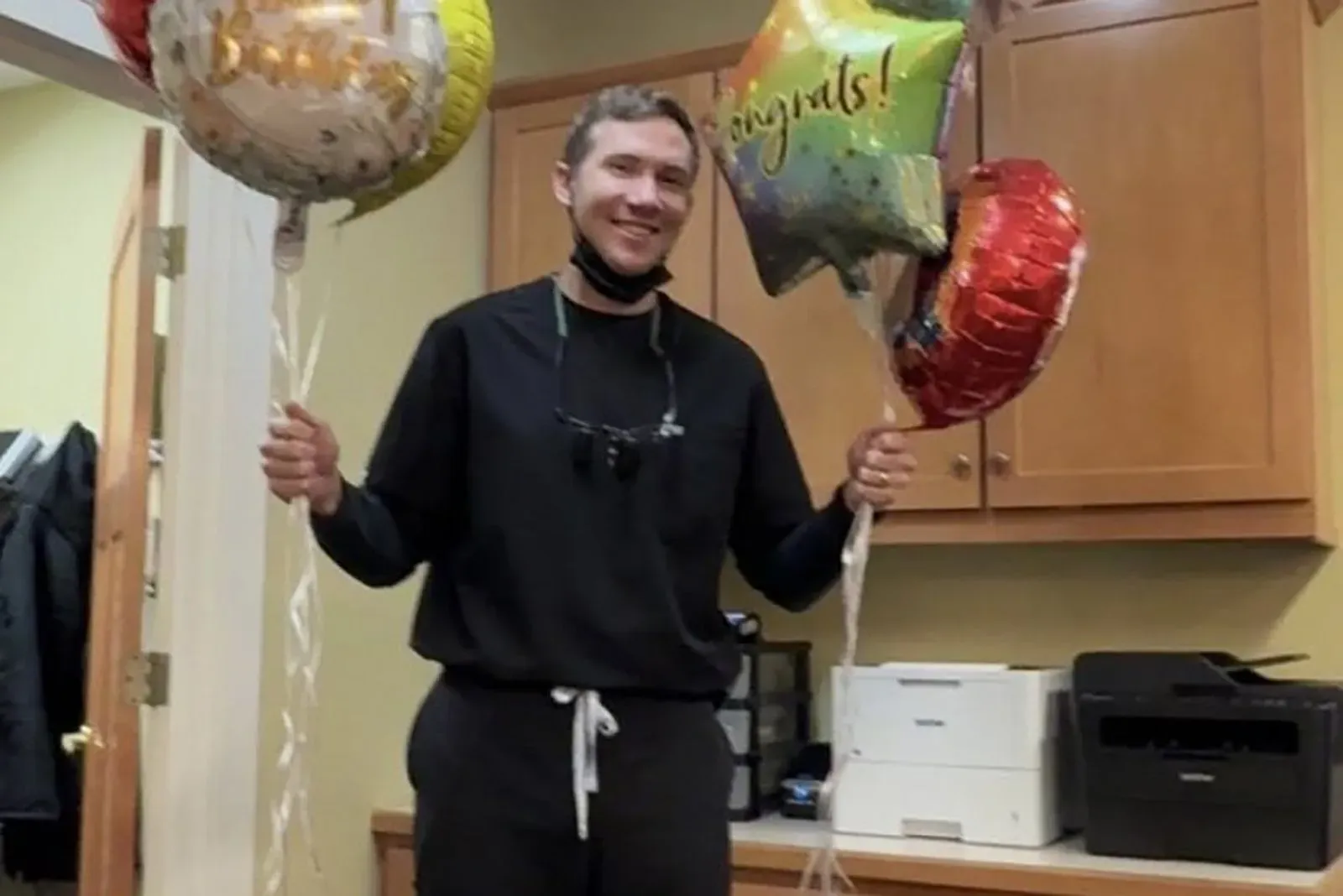 شخص يحمل بالونات ملونة في غرفة مكتب، يعبر عن فرحة أو احتفال، مما يبرز الجانب الإيجابي في حياة طبيب الأسنان سبنسر تيبي.