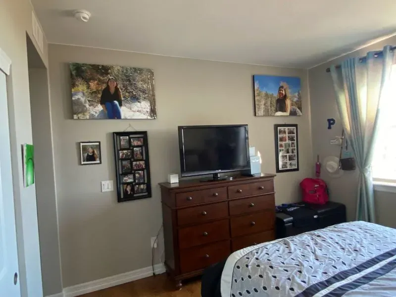 غرفة مراهقة تحتوي على تلفاز وخزانة ومجموعة من الصور على الحائط، تعكس حياة عائلتها وذكرياتها.