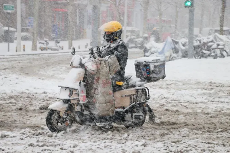 راكب دراجة نارية يرتدي ملابس ثقيلة يسير في عاصفة ثلجية في مدينة جينان، حيث تتساقط الثلوج بغزارة وتتراكم على الطرق.