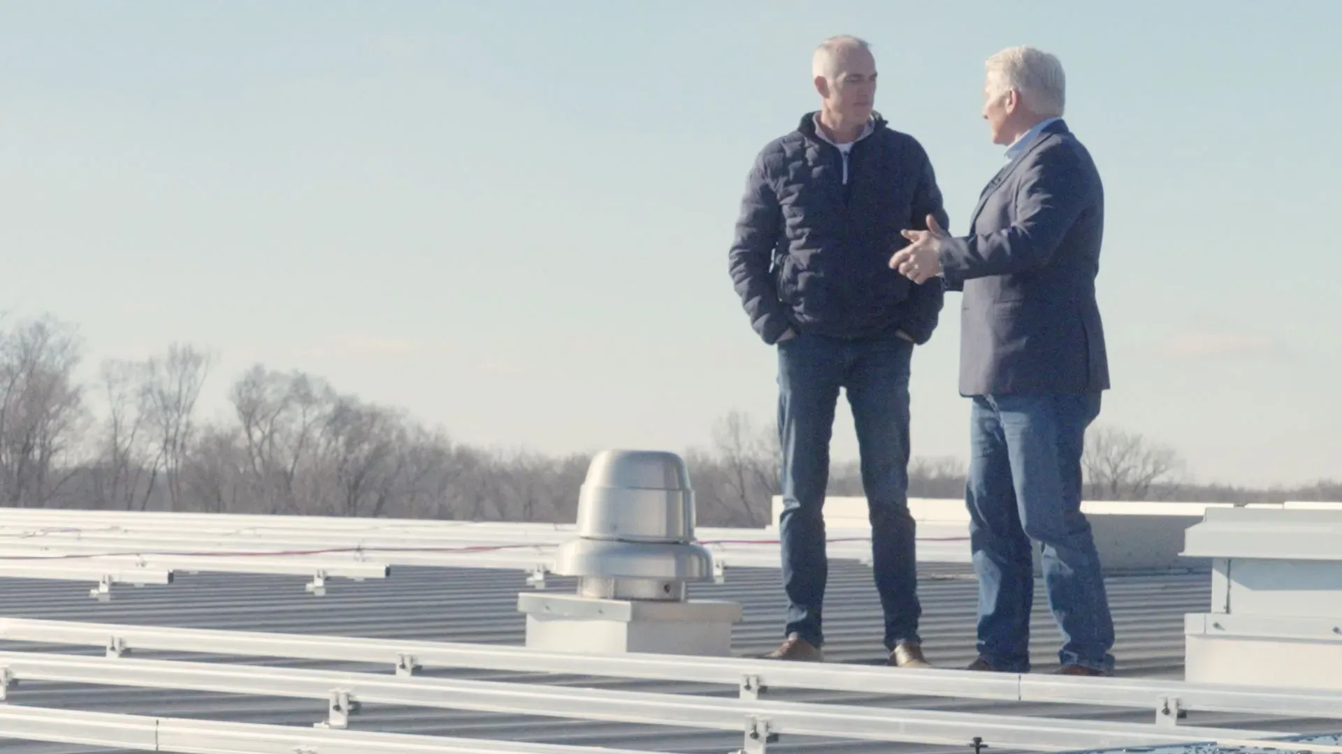 رجلان يتحدثان على سطح مبنى، مع منظر طبيعي خلاب في الخلفية، في سياق مناقشات سياسية حول الانتخابات والمزارع.