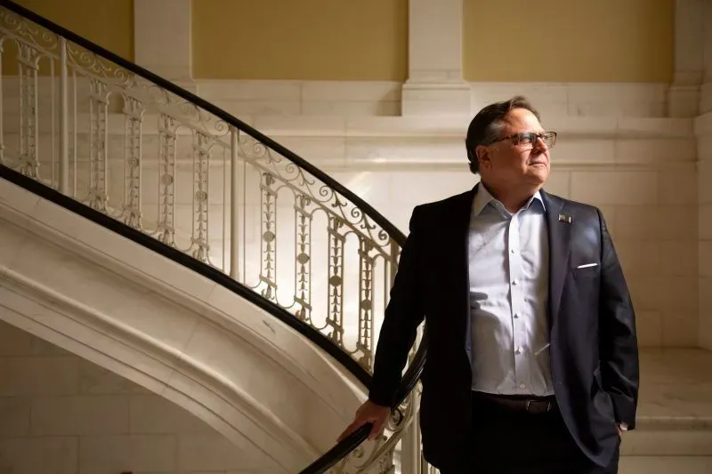 رجل يرتدي بدلة أنيقة يقف على الدرج في مبنى تاريخي، يتأمل بجدية، مما يعكس أجواء التوتر والمأساة المحيطة بقضية اختطاف في واتربري.