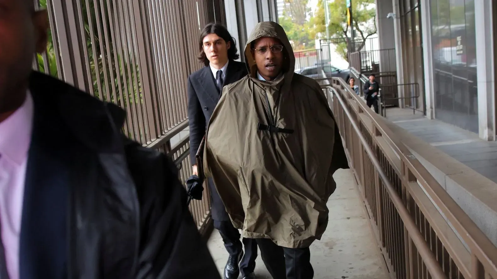 A$AP Rocky يتجول في المحكمة مرتديًا معطفًا واقيًا، برفقة شخص آخر، وسط أجواء من التوتر خلال محاكمته بتهمة الاعتداء.