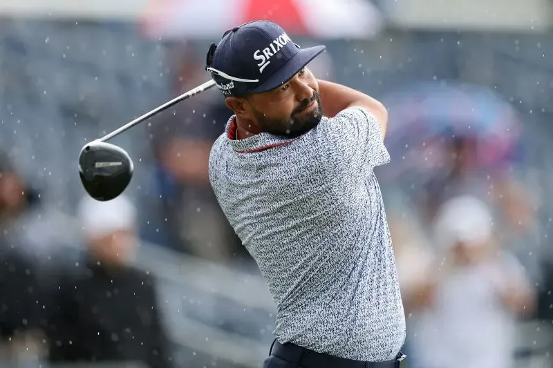 لاعب جولف يسدد الكرة تحت الأمطار في بطولة الولايات المتحدة المفتوحة، مع التركيز على أدائه القوي في الجولة الثالثة.