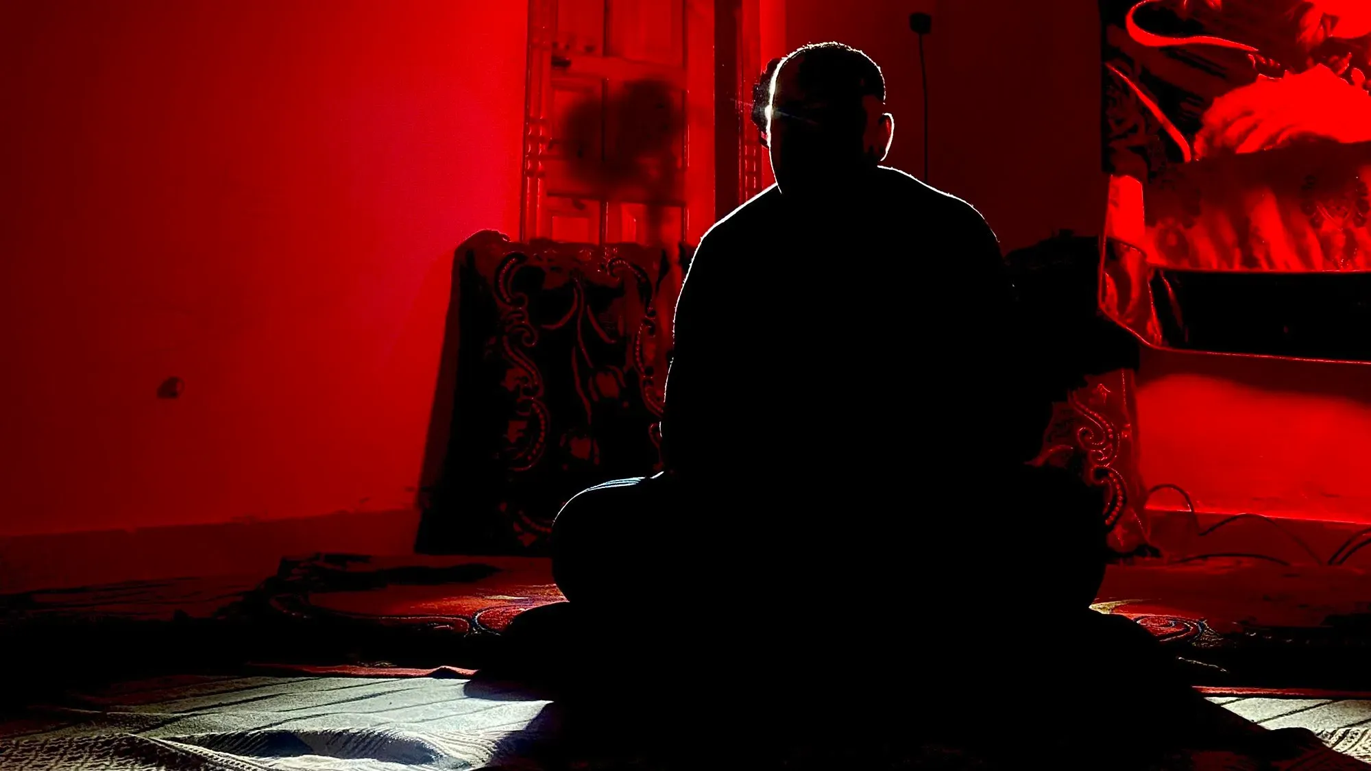 رجل يجلس في غرفة مظلمة بإسلام أباد، مع إضاءة خافتة تبرز ملامحه، يعكس شعور القلق والانتظار بعد انسحاب القوات الأمريكية من أفغانستان.