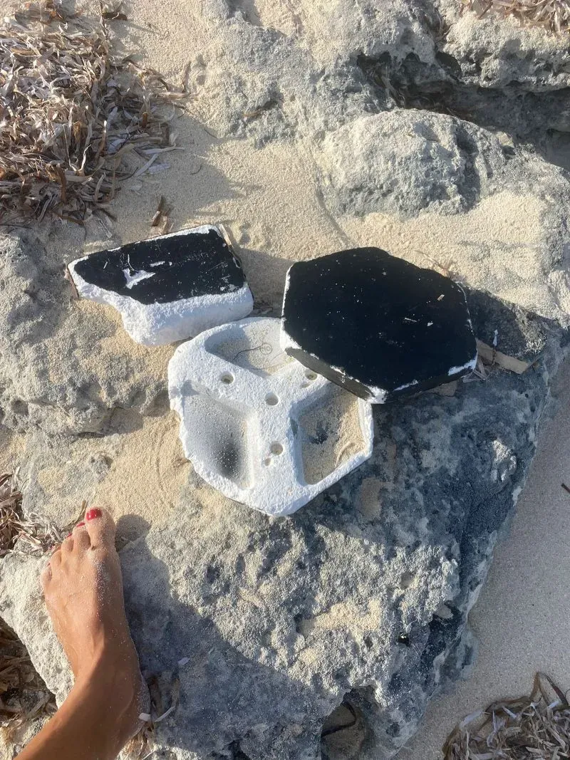 حطام مركبة فضائية يتناثر على الشاطئ في جزر تركس وكايكوس، مع بقايا حرارية على الصخور والرمال، بعد حادثة انفجار المركبة.