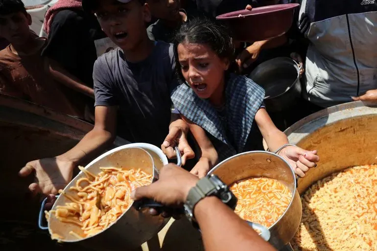 طفلة فلسطينية تعبر عن اليأس أثناء محاولتها الحصول على الطعام في نقطة توزيع مساعدات، وسط تجمع حشود من الناس في غزة.