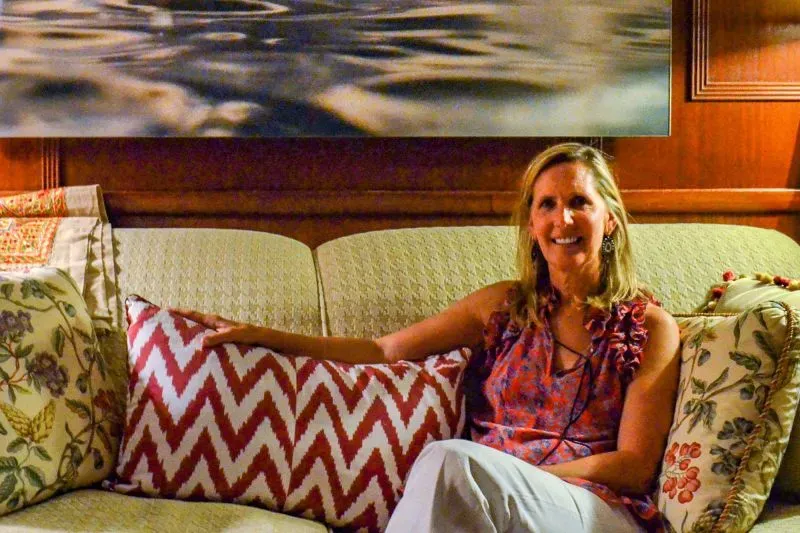 امرأة تجلس على أريكة مزينة، مبتسمة، بينما تظهر خلفها لوحة فنية. تعكس الصورة رحلة تعافيها من مرض الزهايمر.