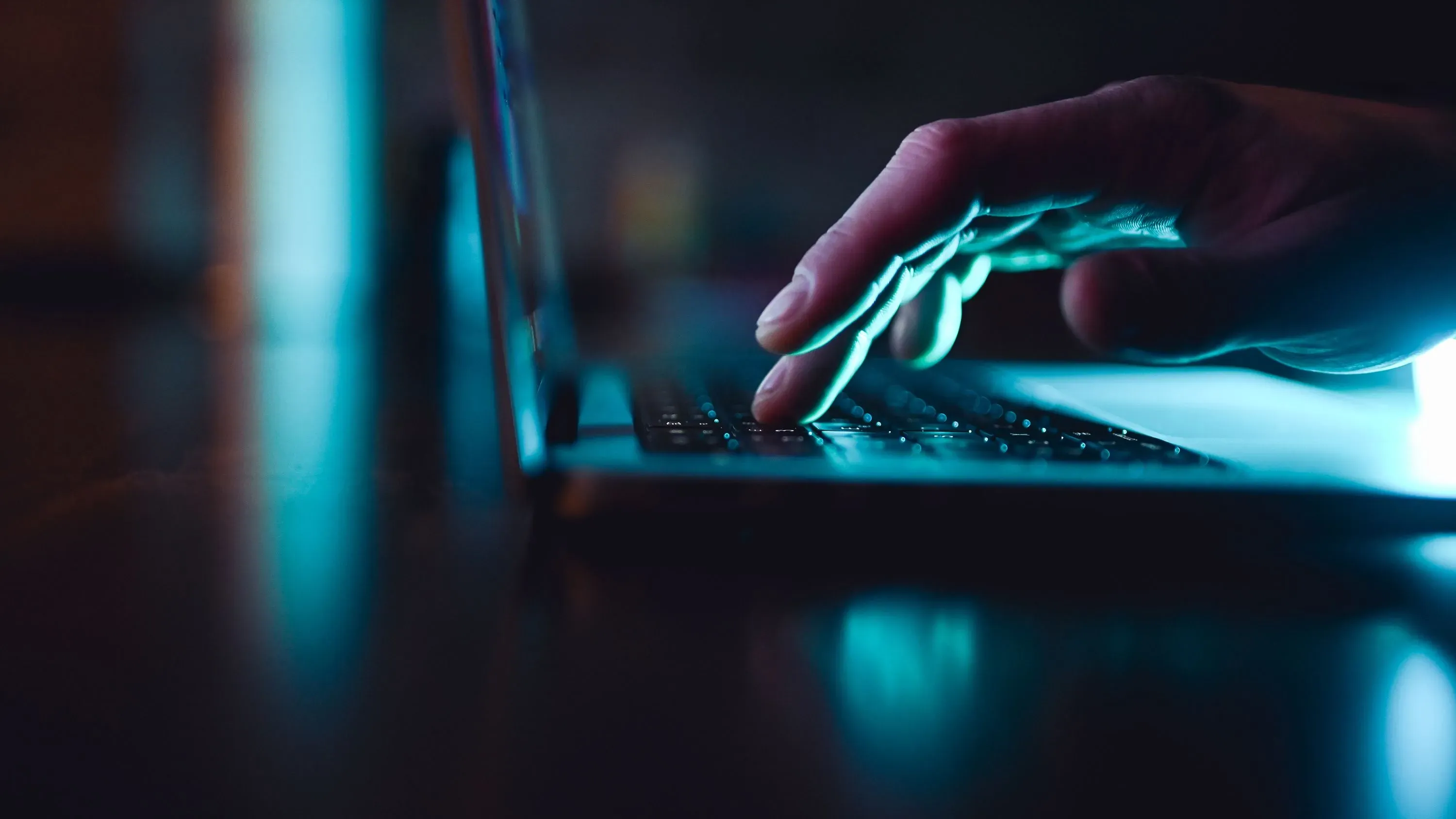 يد لأحد المستخدمين موجهة نحو لوحة مفاتيح جهاز كمبيوتر محمول في بيئة مضاءة بشكل خافت، مما يعكس السهولة في إنتاج المحتوى الرقمي.