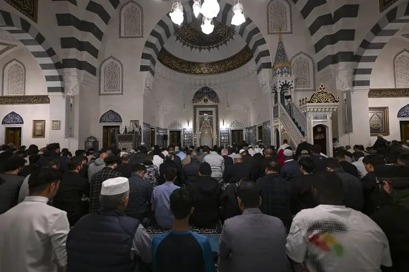 مصلون في مسجد يتجمعون لأداء الصلاة، يظهرون في صفوف مرتبة داخل قاعة مزينة بزخارف إسلامية، مما يعكس أهمية الدين في الحياة العامة.