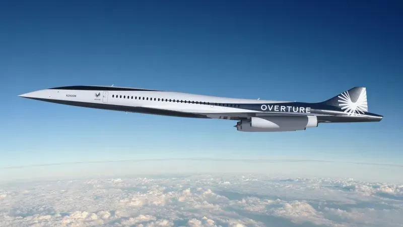 طائرة Overture الأسرع من الصوت تحلق في السماء، مع تصميم انسيابي وألوان زاهية، تمثل مستقبل السفر الجوي.