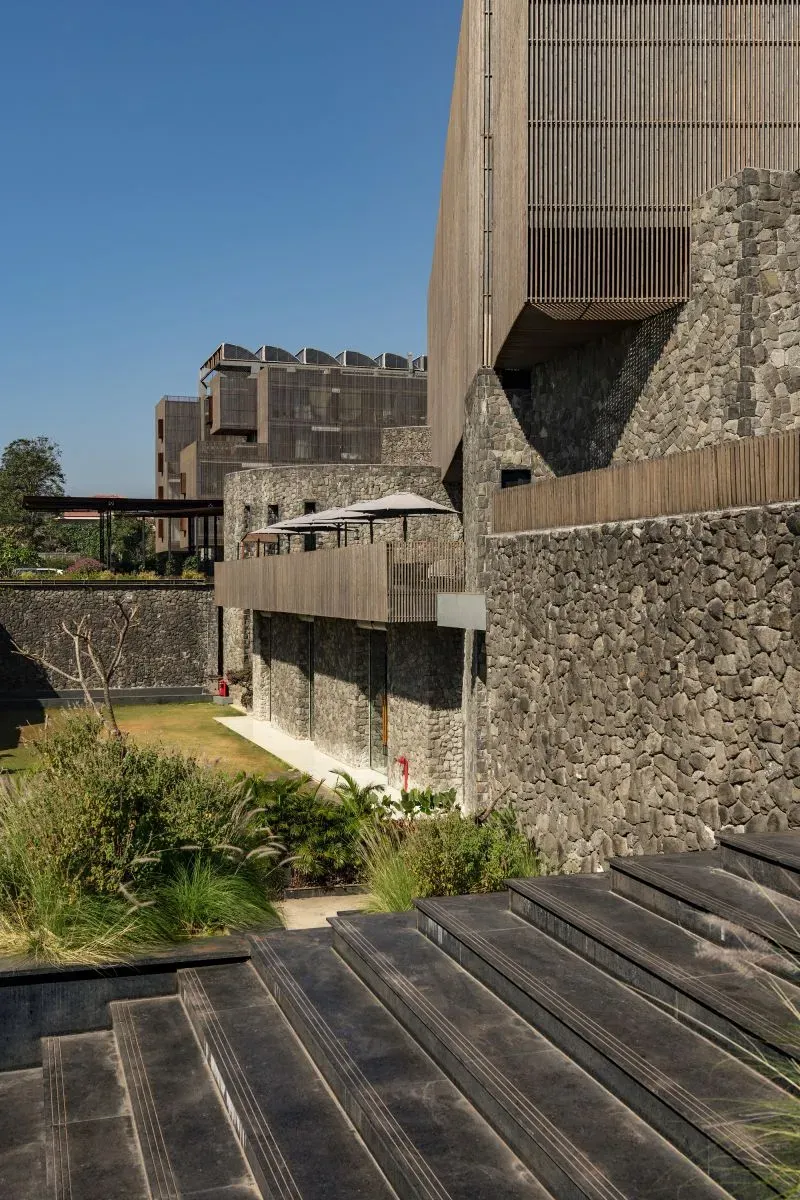 تصميم معماري مبتكر يجمع بين الحجارة البركانية والخشب، مع مساحات خضراء، يعكس مشروع "لافا فورمينغ" لاستغلال الحمم البركانية في البناء.