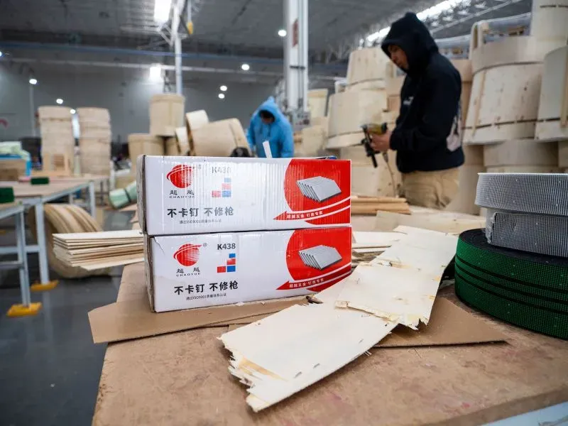 مجموعة من الصناديق والخشب في مصنع صيني صناعي بالمكسيك، مع عمال يرتدون ملابس دافئة، مما يعكس النمو الصناعي والتعاون بين الثقافتين.