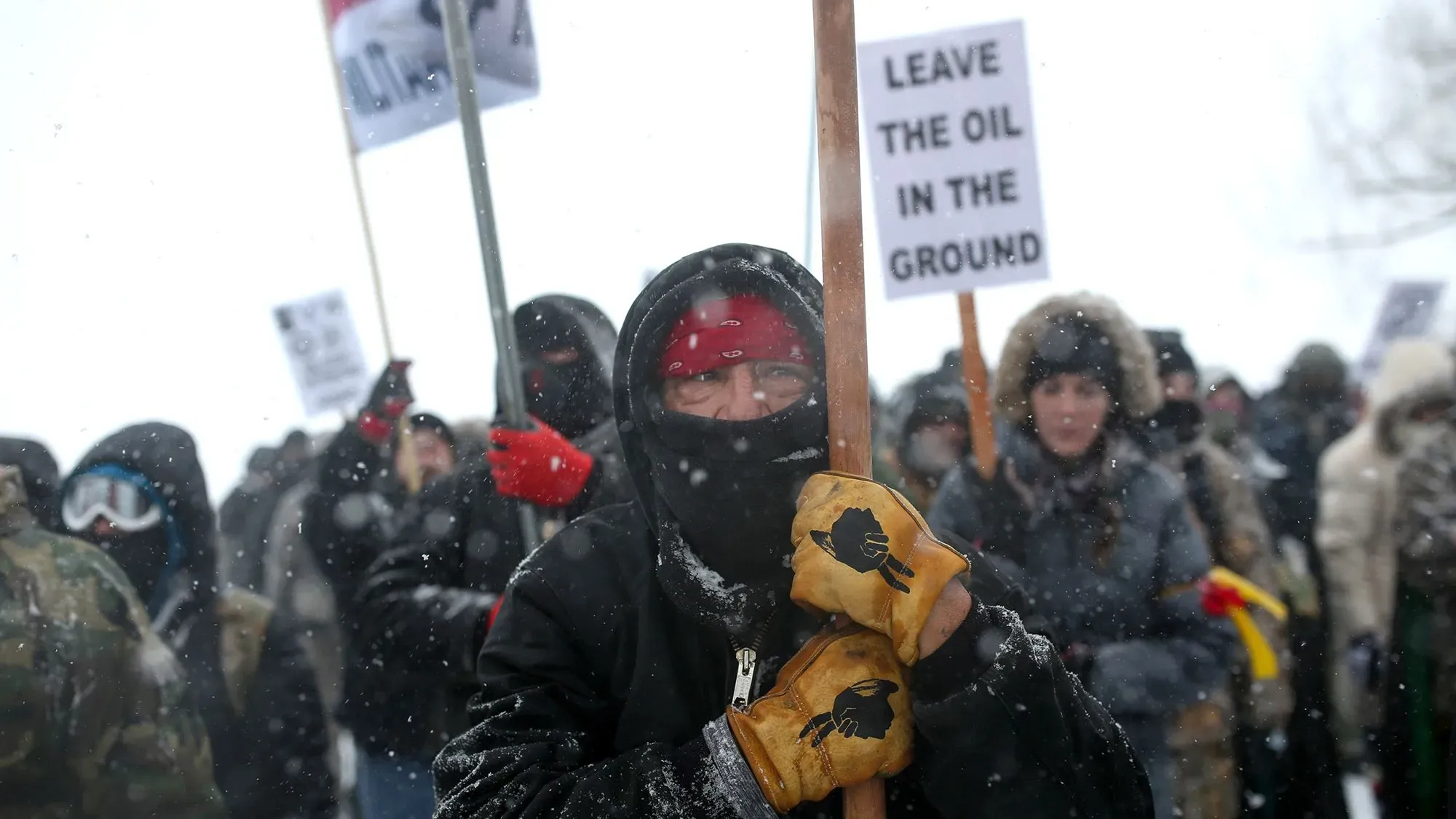 محتج يرتدي ملابس شتوية ويحمل لافتة كتب عليها "اتركوا النفط في الأرض"، وسط مجموعة من المحتجين خلال احتجاجات خط أنابيب داكوتا أكسيس.
