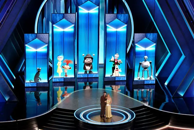 غولدي هاون وأندرو غارفيلد يقفان على المسرح في حفل الأوسكار، مع شخصيات كرتونية ملونة خلفهما، أثناء تقديم جوائز الأفلام.