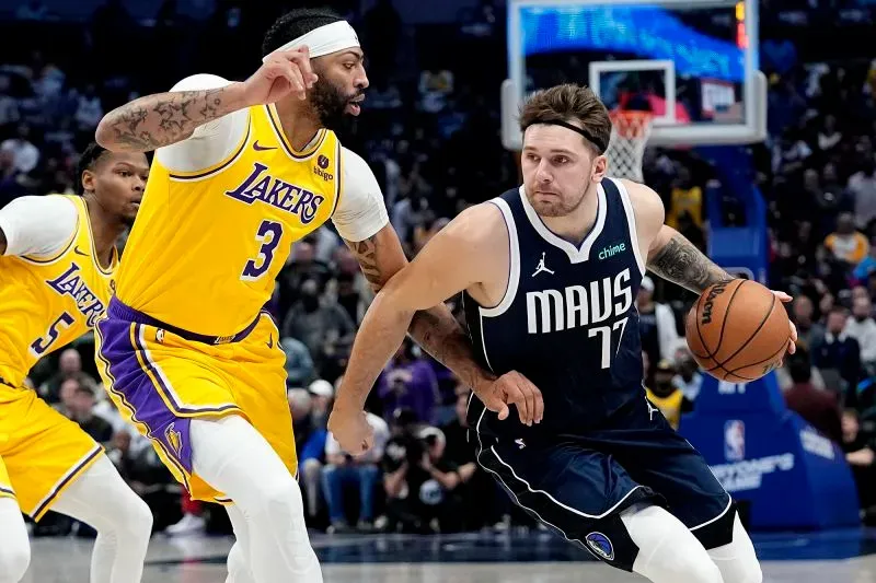 أنتوني ديفيس، لاعب كرة السلة، يتنافس مع لوكا دونشيتش، بينما يرتدي ديفيس زي لوس أنجلوس ليكرز ودونشيتش زي دالاس مافريكس.