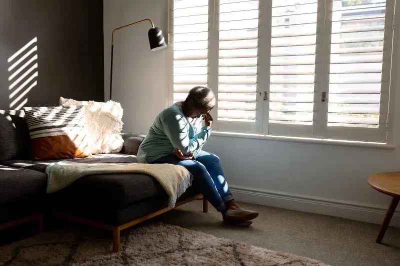 امرأة تجلس على أريكة في غرفة مضيئة، تعبر عن مشاعر الحزن والتفكير العميق، مما يعكس تأثير الاكتئاب على مرضى الخرف.