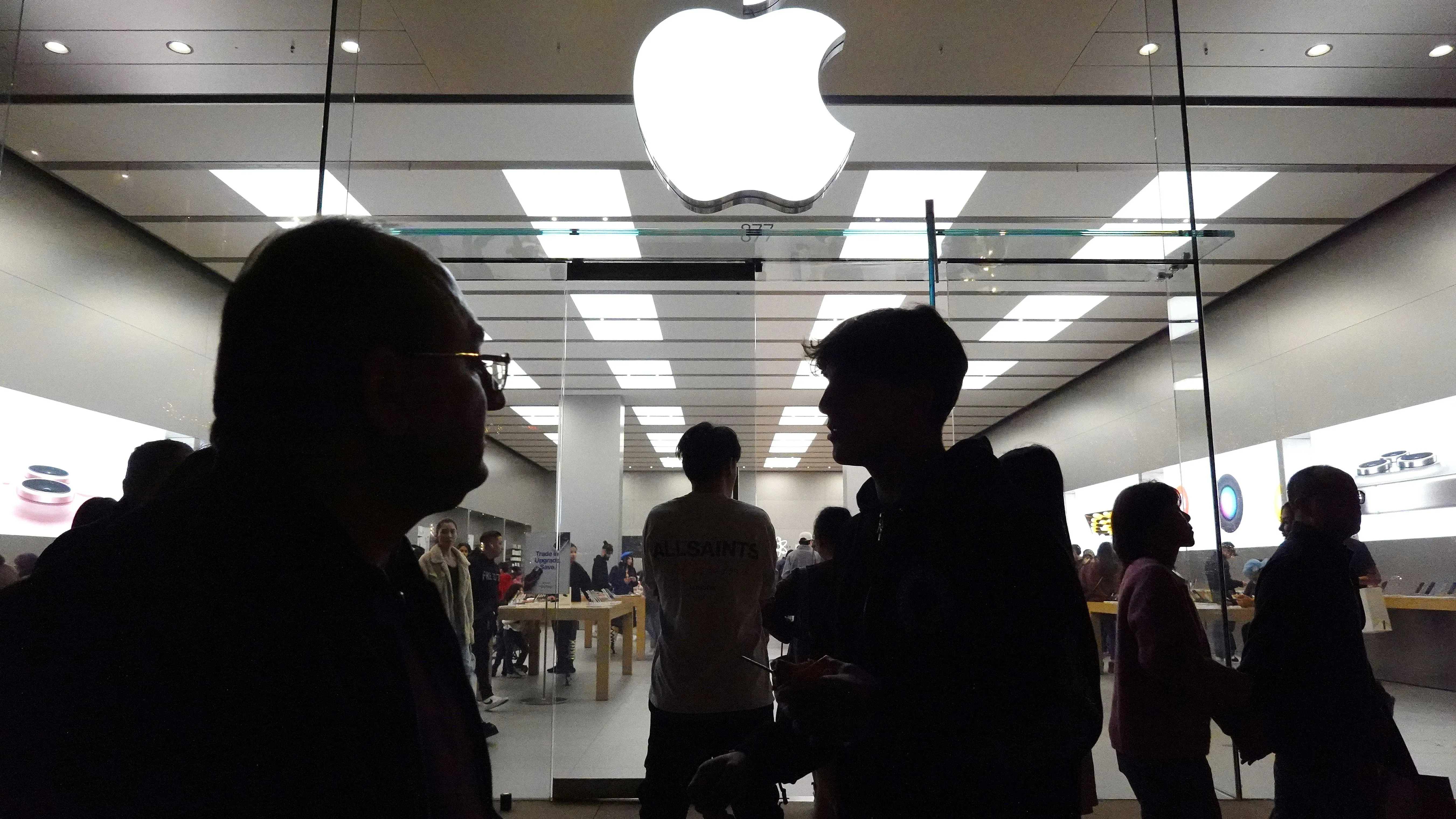 جمهور ينتظر دخول متجر أبل، مع ظهور شعار أبل في الخلفية، مما يعكس إطلاق iPhone 16e الجديد.