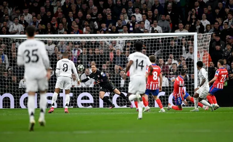 لاعبو ريال مدريد في مواجهة أتلتيكو مدريد خلال مباراة دوري أبطال أوروبا، مع لحظة تسديدة على المرمى وسط حماس الجماهير.