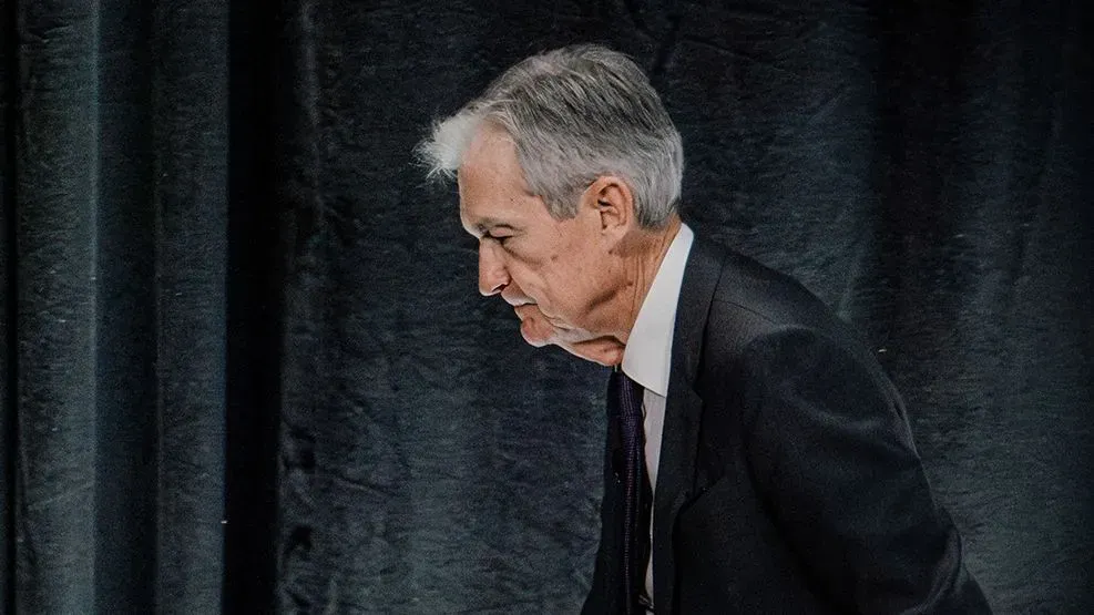 جيروم باول، رئيس الاحتياطي الفيدرالي، يغادر منصة الخطابة، معبرًا عن التوترات الاقتصادية وسط انتقادات ترامب لسياساته المالية.