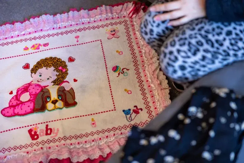 بطانية مزينة برسمة لطفلة مع كلب، بينما تجلس فتاة صغيرة على الأرض. تعكس الألوان الزاهية أجواء الطفولة والبراءة.