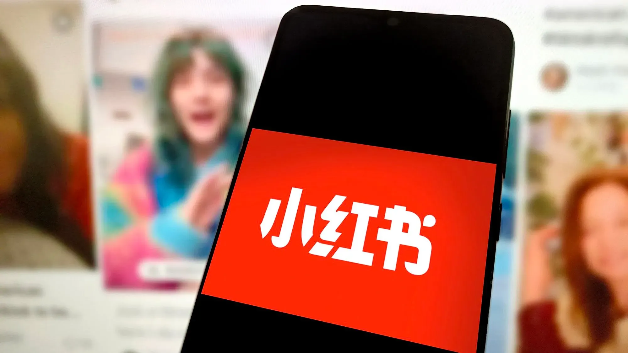 شعار منصة Xiaohongshu (RedNote) يظهر على شاشة هاتف ذكي، مع محتوى مستخدمين في الخلفية، في سياق تدفق المستخدمين الأمريكيين الجدد.