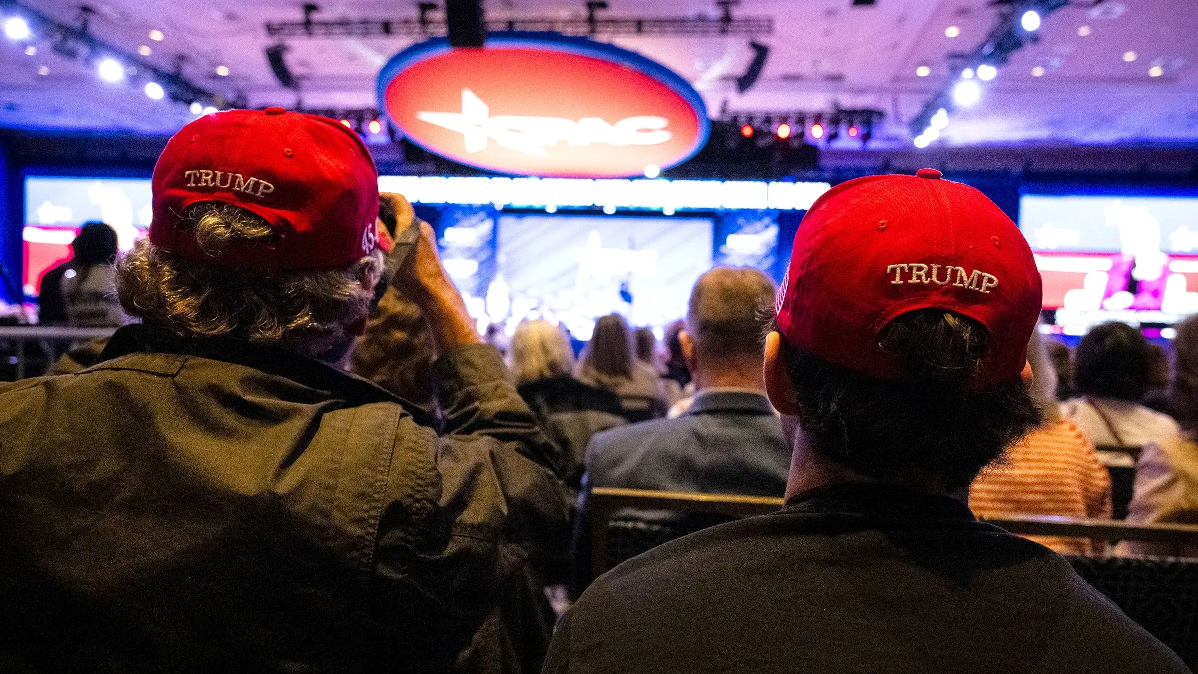 حضور مؤيدي ترامب في مؤتمر "CPAC" يرتدون قبعات حمراء تحمل اسم ترامب، مع خلفية من الأضواء والشاشات، تعكس التوتر بين الحركة المحافظة وشركات التكنولوجيا.