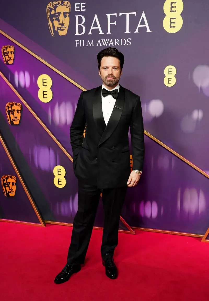 ممثل يرتدي بدلة سوداء أنيقة يقف على السجادة الحمراء خلال حفل جوائز BAFTA، مع خلفية تحمل شعار الجائزة.