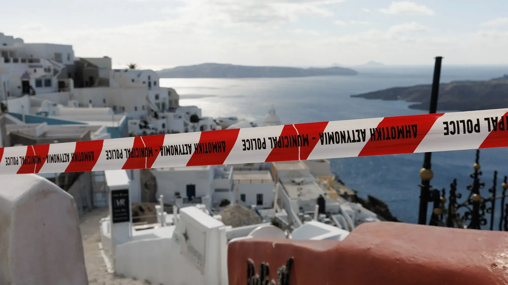 سياج أمني بألوان تحذيرية يحيط بمنطقة في سانتوريني، مع منظر للبحر والجزر المجاورة، في ظل حالة الطوارئ بسبب النشاط الزلزالي.