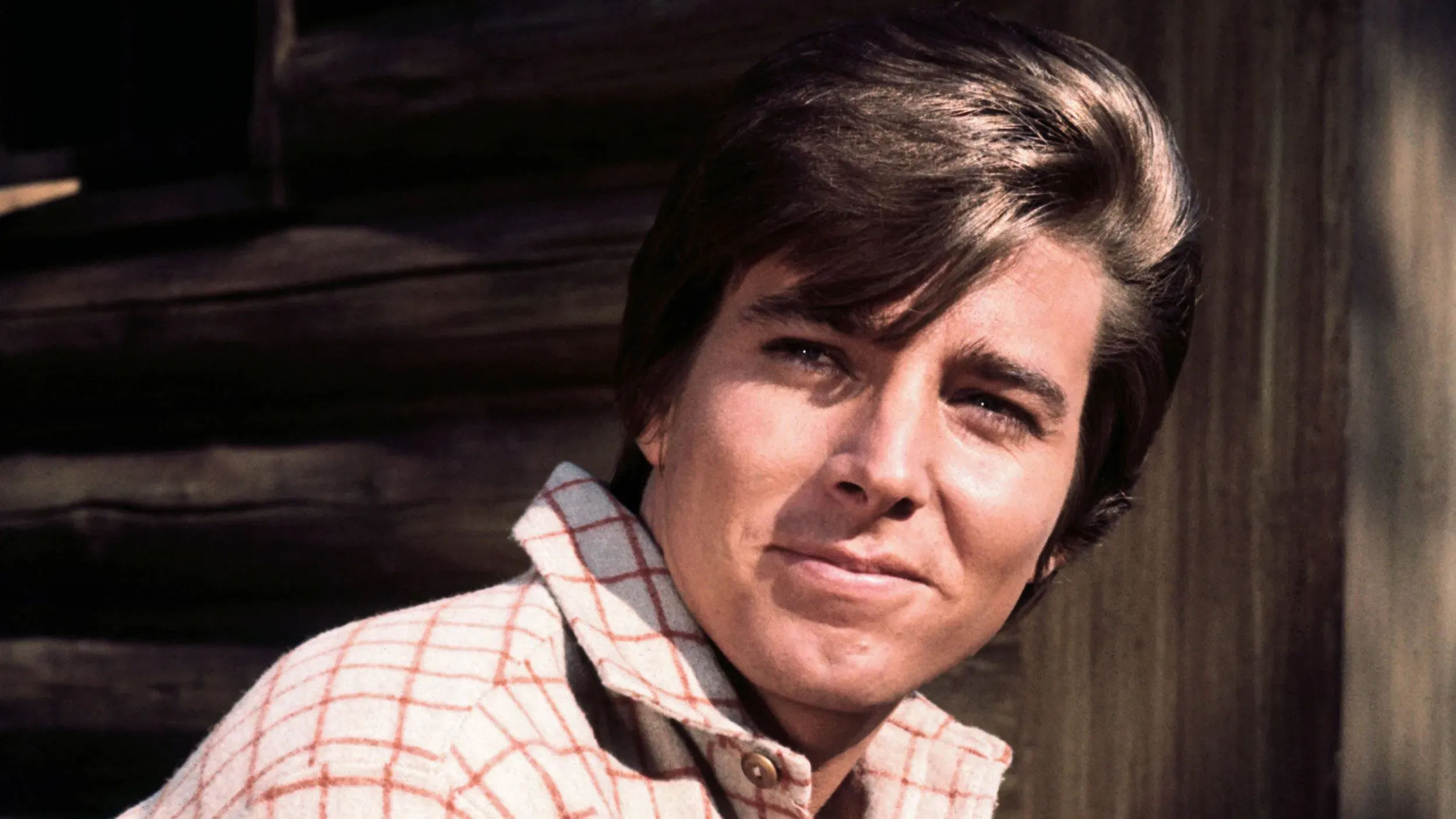 بوبي شيرمان، نجم الستينيات والسبعينيات، مبتسمًا بشعره الأنيق، معلقًا في خلفية خشبية، يمثل جيلًا من معجبي الموسيقى والتلفزيون.