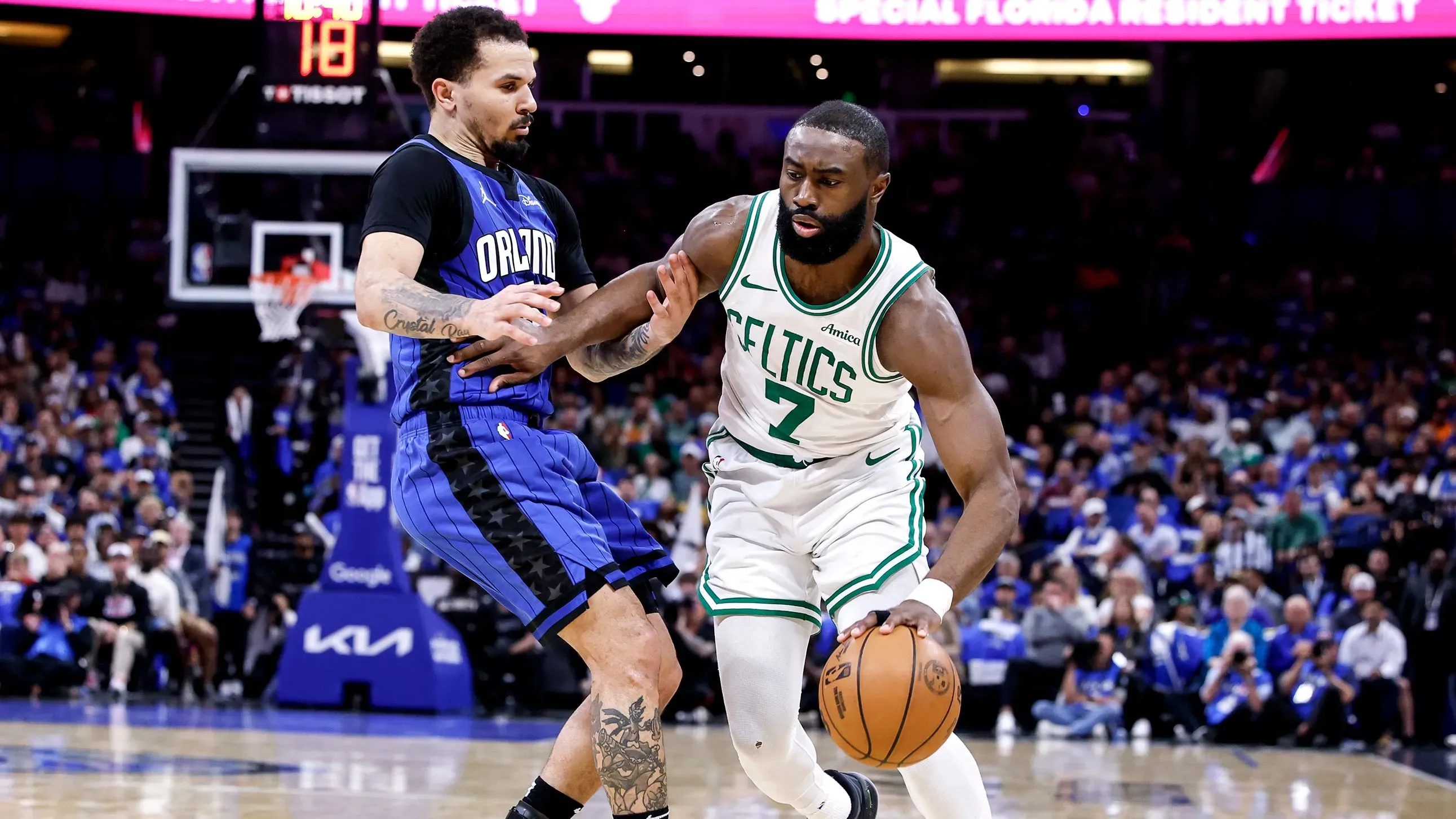 جايلين براون من فريق بوسطن سيلتيكس يتجاوز كول أنتوني من فريق أورلاندو ماجيك أثناء مباراة كرة السلة، مع وجود جمهور في الخلفية.