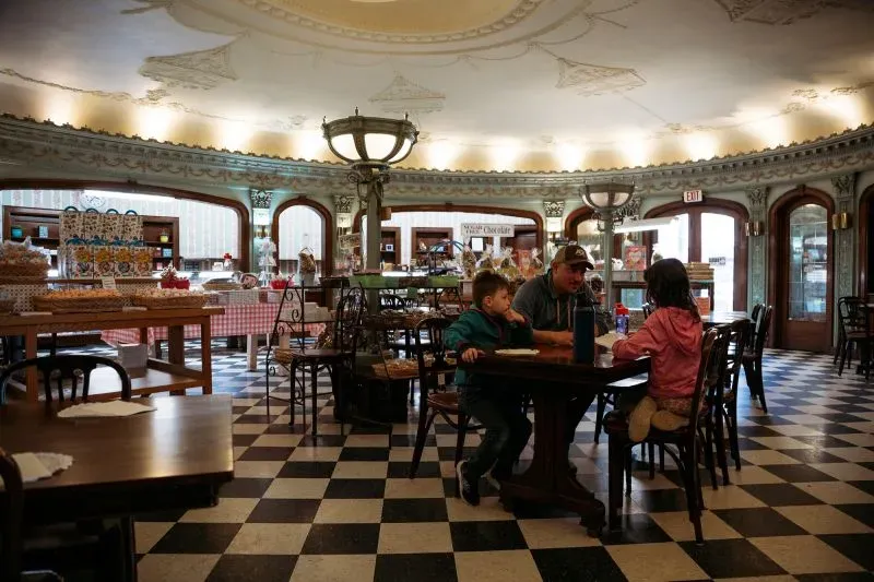 داخل مطعم تقليدي في بافالو، يجلس أب مع طفلين على طاولة مستديرة، محاطين بديكور آرت ديكو وأجواء دافئة.