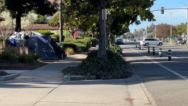 خيمة مشردين على رصيف في مدينة فريمونت بكاليفورنيا، تعكس التحديات المتزايدة المتعلقة بالتشرد والسياسات الجديدة التي تجرم المساعدة.