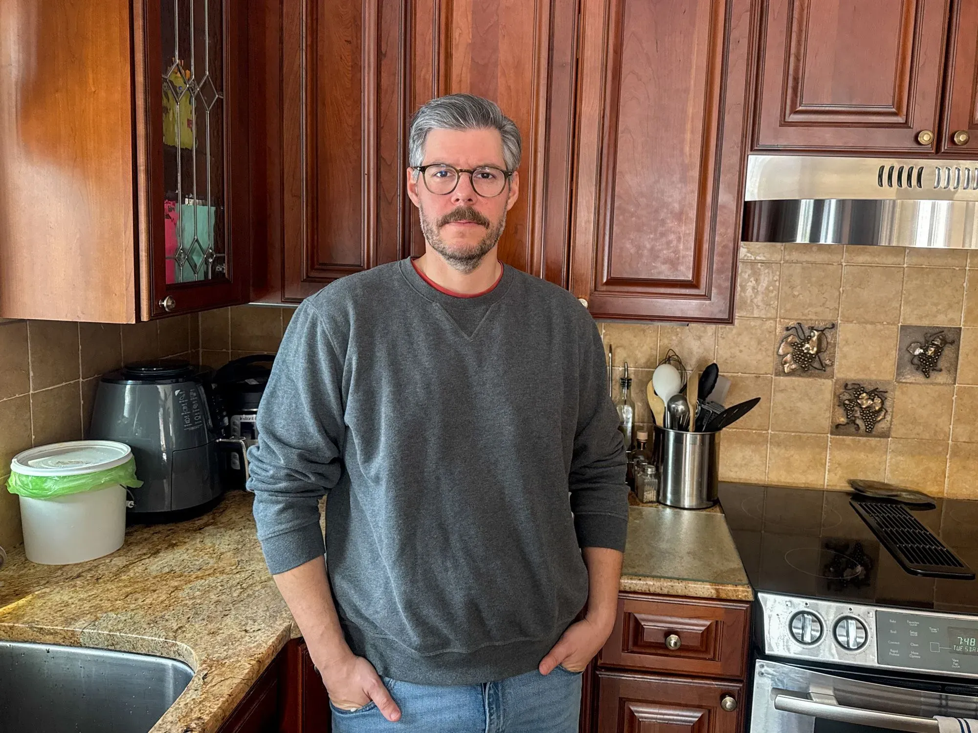 رجل في المطبخ يقف بجانب حوض الغسيل، يعبر عن مشاعر الإحباط من توزيع الأعمال المنزلية غير المتكافئ.