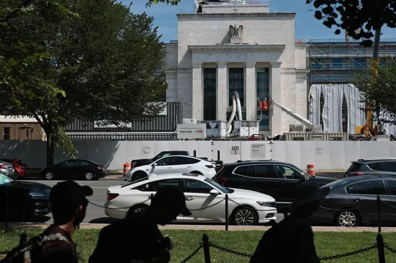 مبنى الاحتياطي الفيدرالي في واشنطن أثناء أعمال التجديد، مع ظهور سيارات ومشاريع بناء خلفية، مما يبرز التكاليف المرتفعة للمشروع.