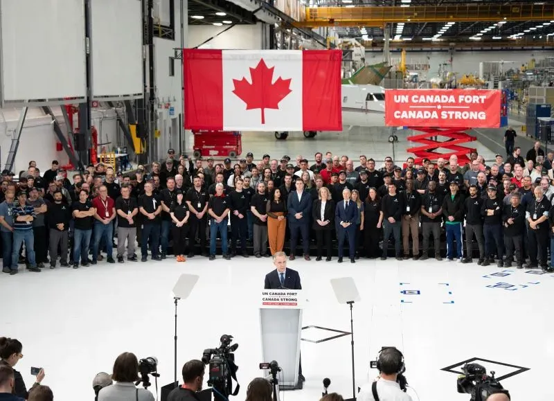 رئيس الوزراء مارك كارني يتحدث أمام حشد من العمال في مصنع، مع العلم الكندي خلفه، خلال حملة انتخابية وسط التوترات التجارية مع الولايات المتحدة.