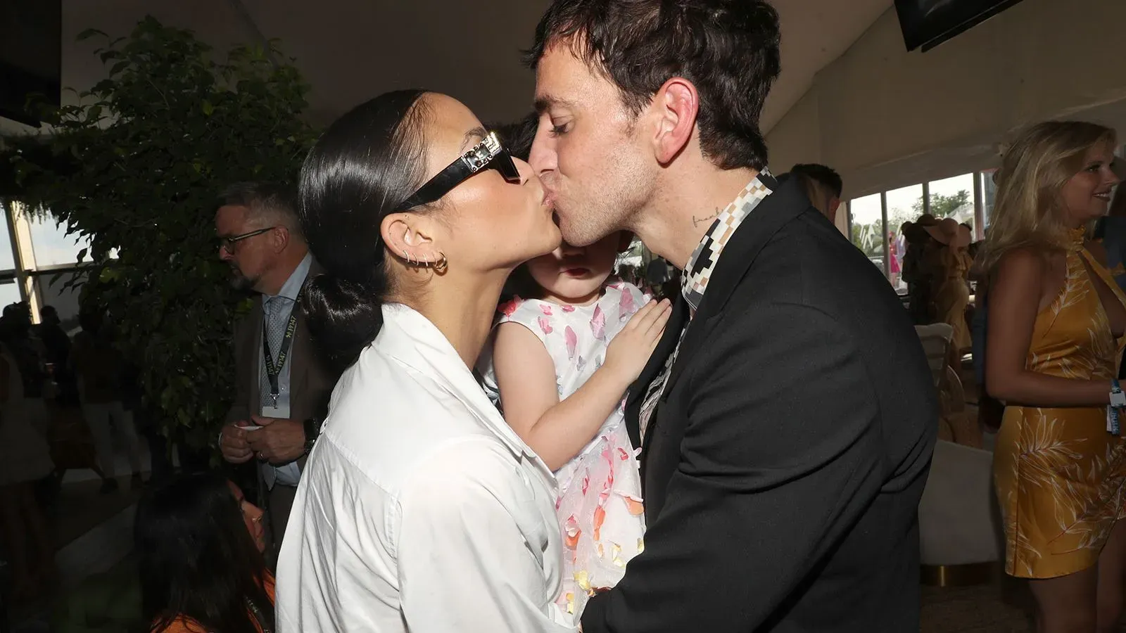 قبلات حميمية بين كاسي فينتورا وزوجها أليكس فاين في مناسبة عائلية، مع وجود طفلتهما في حضن فاين، يعكسان الحب والدعم المتبادل بينهما.