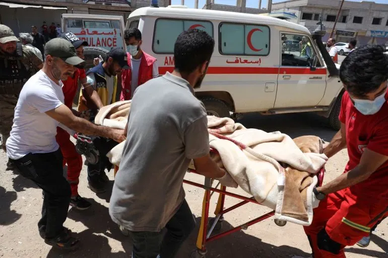 أفراد من فرق الإسعاف يحملون مصابًا مغطىً ببطانية في مدينة السويداء، مع وجود سيارة إسعاف في الخلفية، وسط تصاعد العنف.