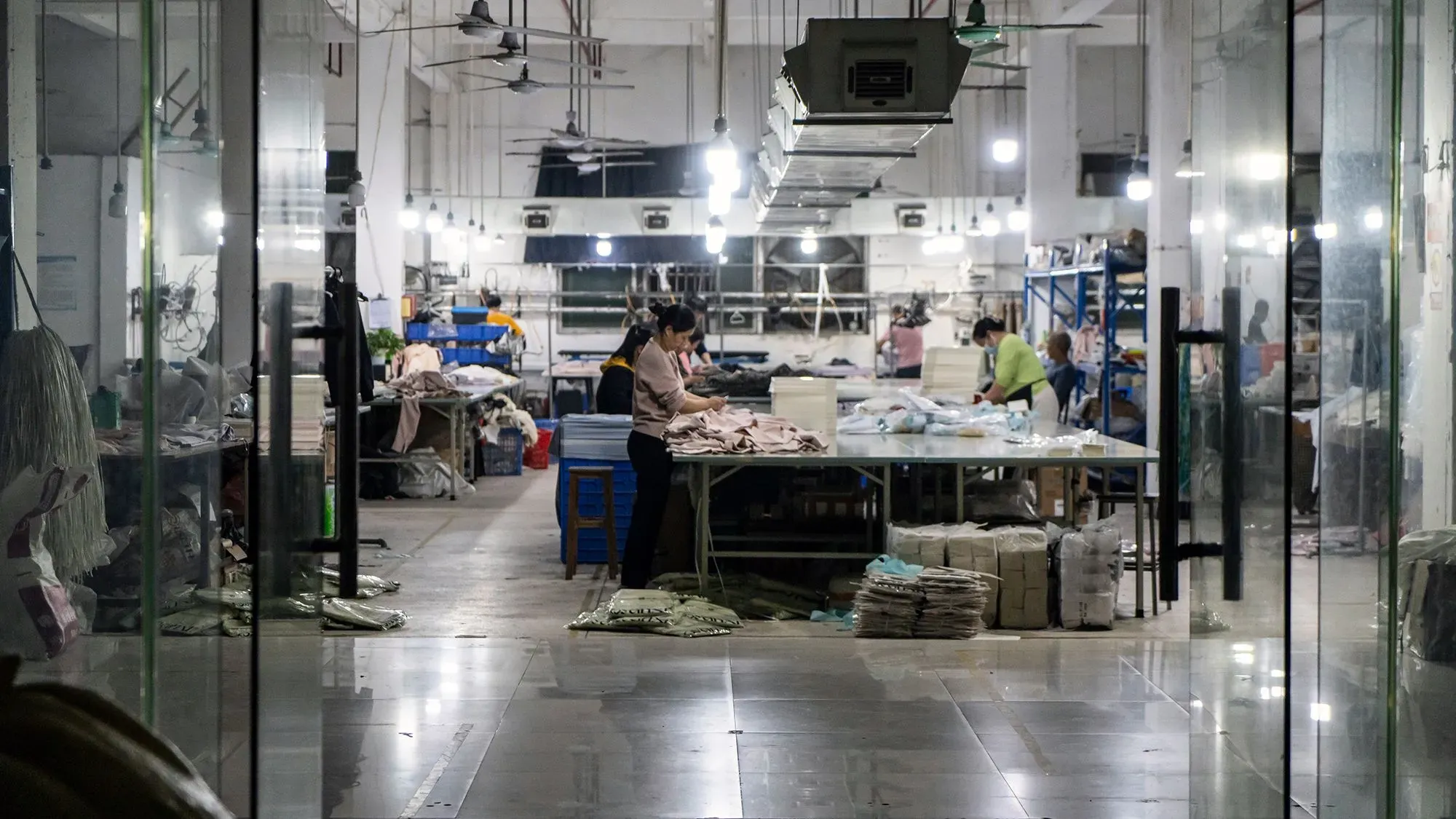 صورة لمصنع ملابس داخلي حيث يعمل العمال على تجهيز الملابس. يبرز في الخلفية أرفف مليئة بالمنتجات، مما يعكس عمليات التصنيع السريعة.